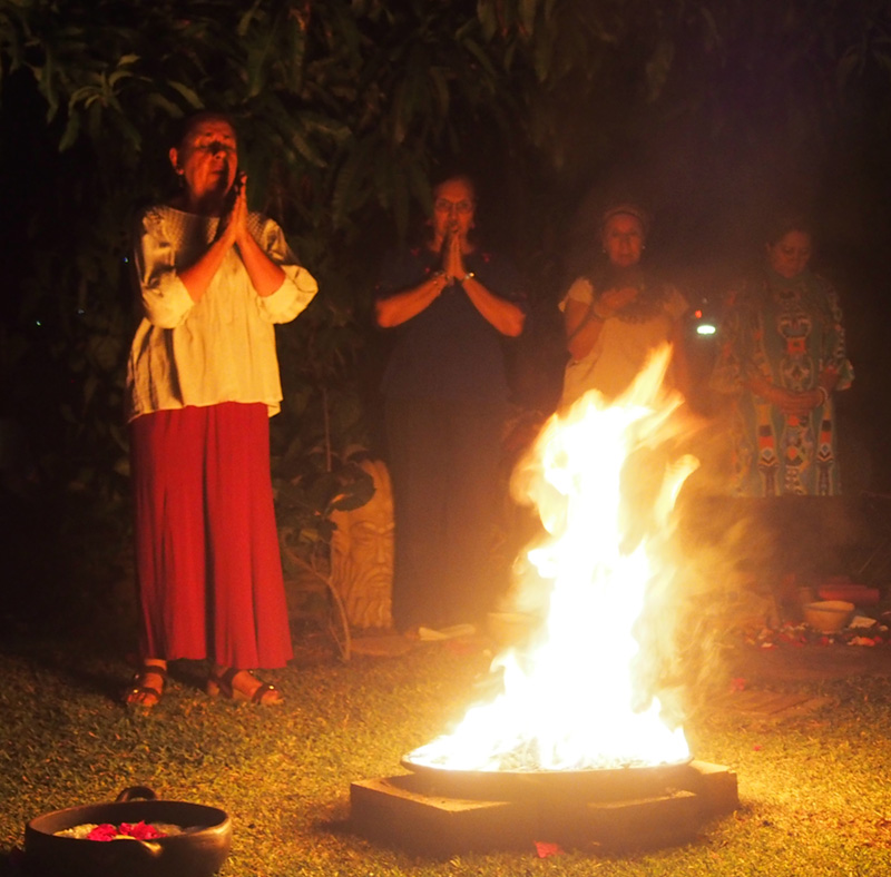 Elder woman praying in front of the sacred fire in a healing ceremony with more people with devotion 